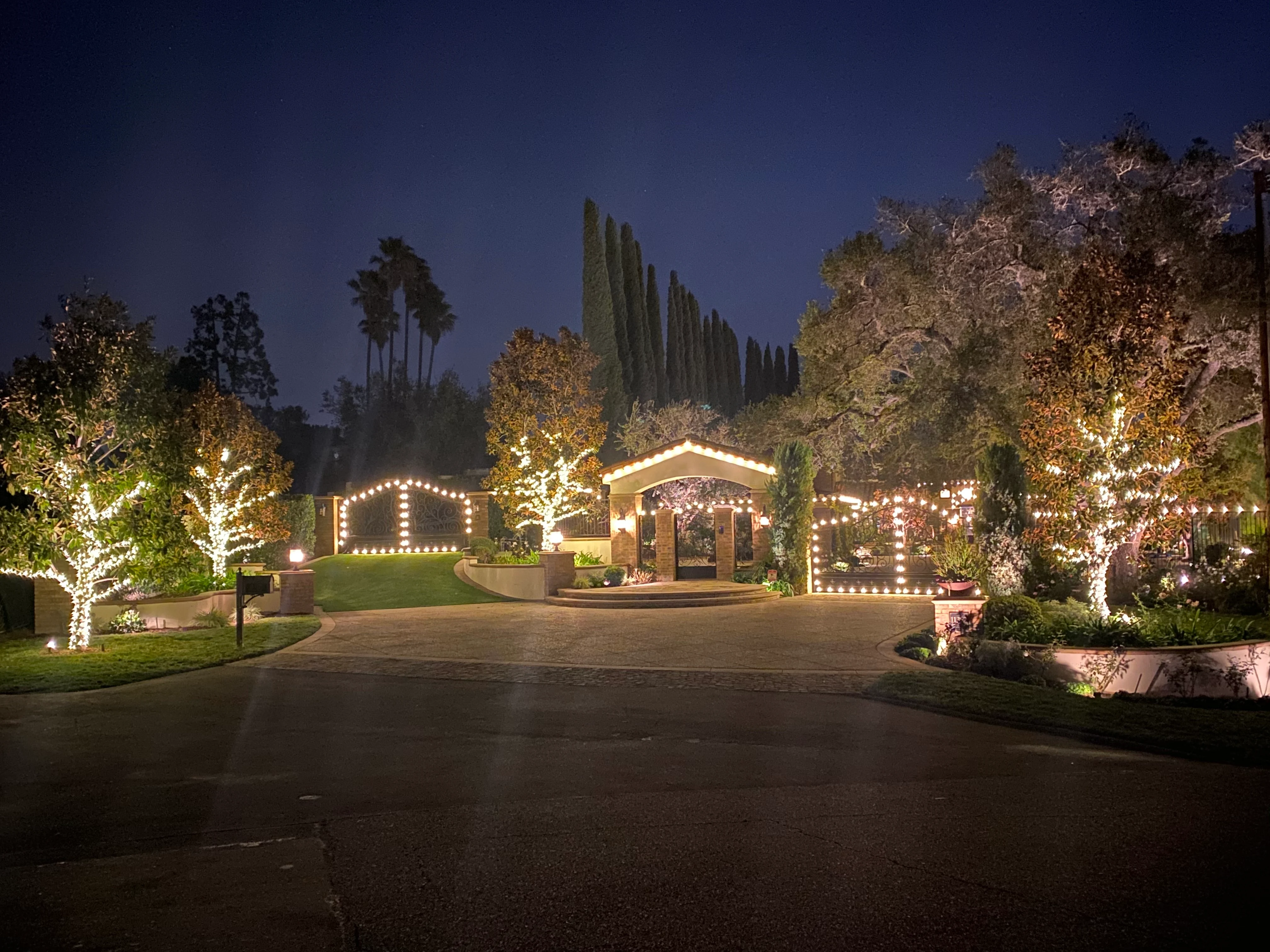 Temecula estate entry with warm roofline holiday lighting at dusk